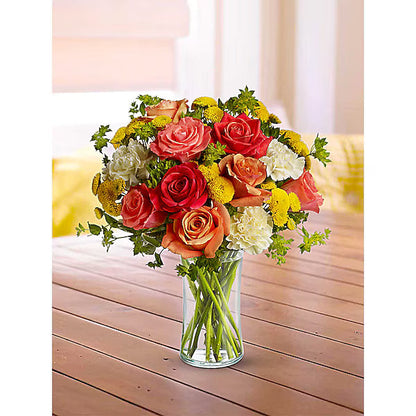 Red, orange, and yellow flower bunch in clear vase on wooden tabel