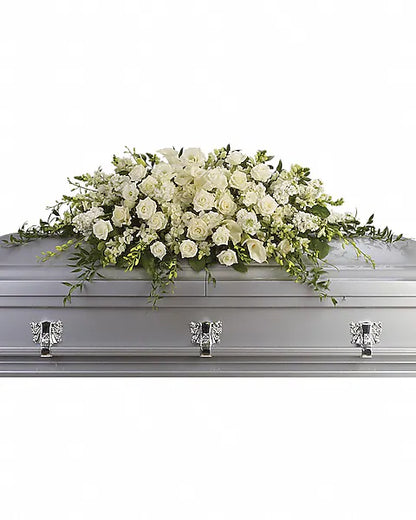 Silver coffin topped with fresh flowers on white background
