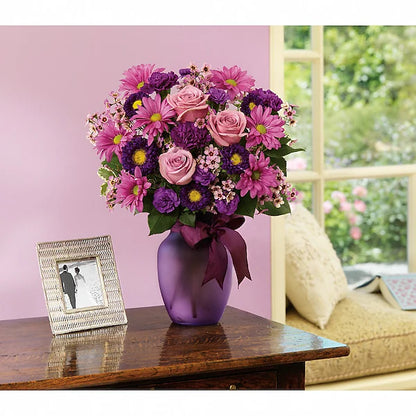 Purple vase of flowers on wooden table against pink wall