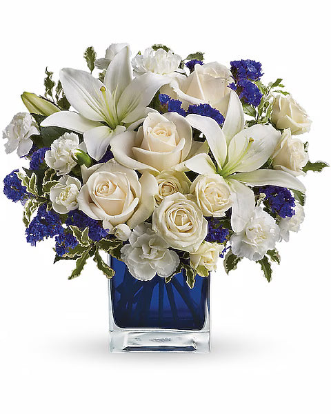 Floral arrangement with white flowers and blue accents in a blue vase on a white background