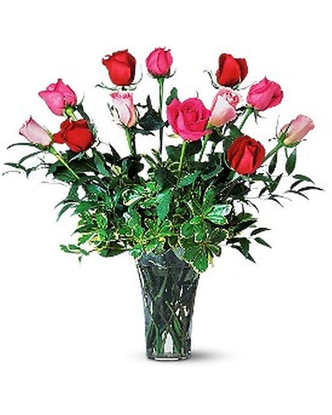 Bouquet of red, pink, and white roses in a clear vase on a white background